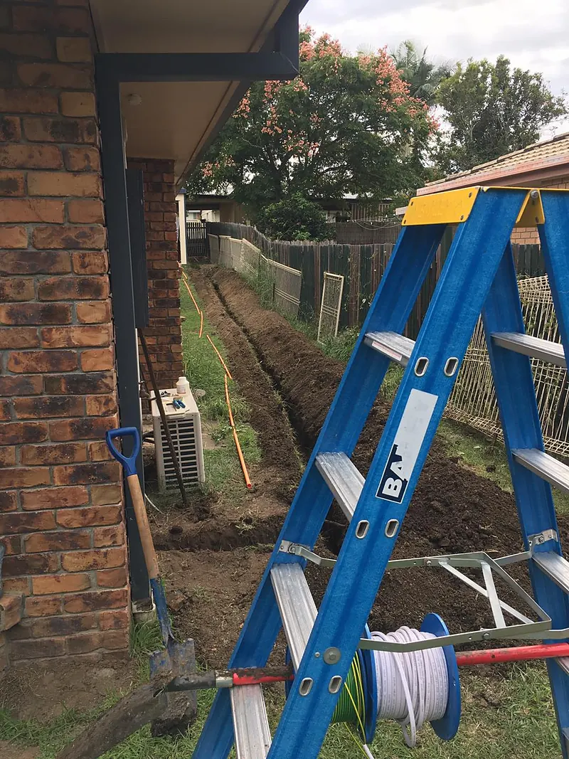 Trench dug beside a brick house for an underground cable run